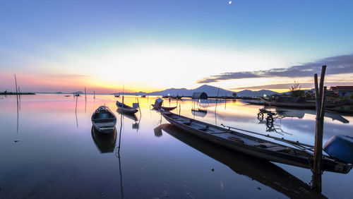 Sailboats moored in lake against sky during sunset