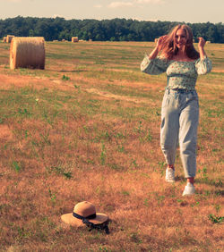 A young girl's hat fell out in a field with hay bales