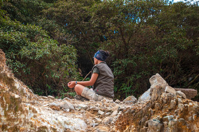 Side view of man sitting on rock in forest