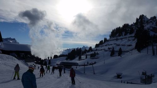 People skiing on snowcapped mountains against cloudy sky