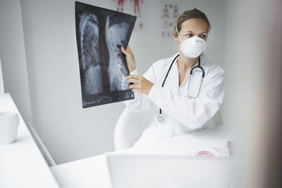 Female doctor wearing mask holding medical x-ray in hospital