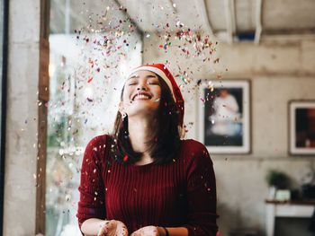 Close-up of smiling young woman throwing confetti while standing at home during christmas