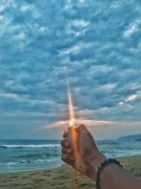 Person holding camera on beach against sky