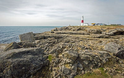 Lighthouse on rocks by sea against sky