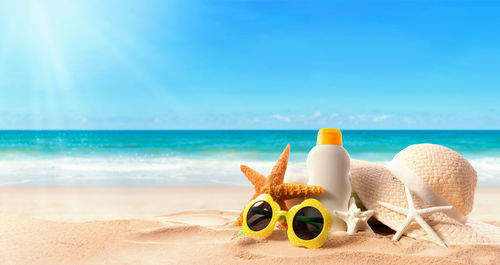 Close-up of sunglasses and hat on beach against sky