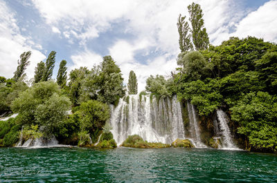 Scenic view of waterfall in forest against sky