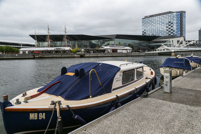 Boats moored at harbor against sky in city