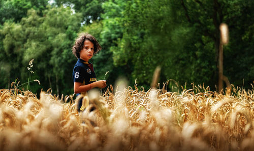 Portrait of cute boy standing on land against trees