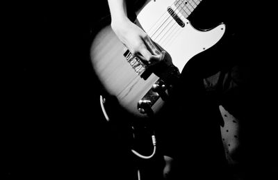 Close-up of hands playing guitar against black background