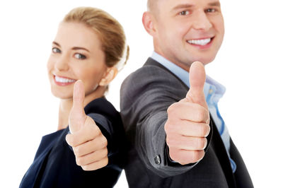 Portrait of smiling colleagues gesturing thumbs up sign against white background