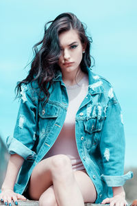 Portrait of young woman sitting against blue background