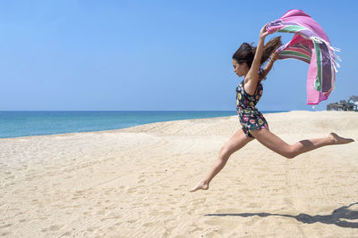 Full length of girl jumping with fabric at beach