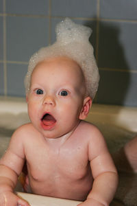 Close-up of surprised shirtless baby boy with soap sud on head in bathtub