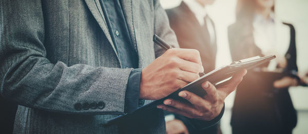 Midsection of businessman writing on document in office