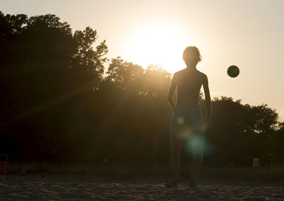 Rear view of woman standing on field against sky during sunset