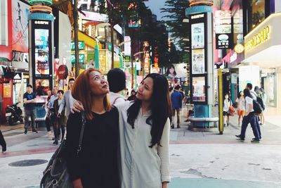 Mother and daughter with arm around standing in market at dusk