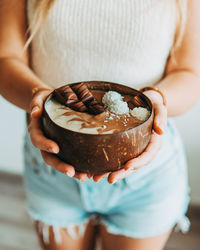 Midsection of woman holding breakfast in coconut bowl at home