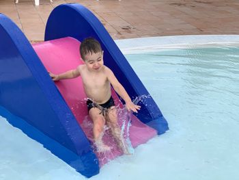 High angle view of shirtless boy sliding in swimming pool