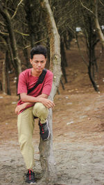 Portrait of young man leaning against tree trunk