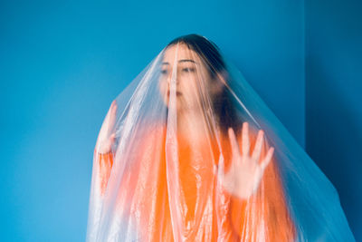 Teenage girl wrapped in plastic against blue background