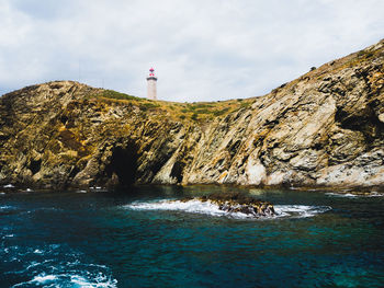 Lighthouse on rock by sea against sky