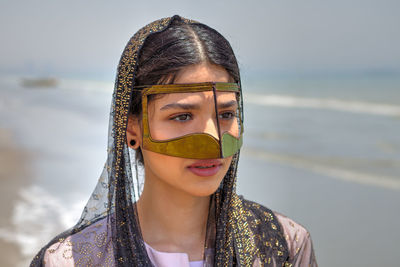 Close-up of young woman wearing traditional clothing standing at beach against sky