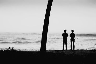 People standing on beach against clear sky