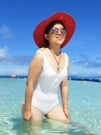 Smiling woman wearing hat while standing in sea