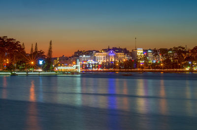 Illuminated buildings by river against sky at night