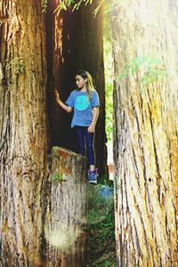 Full length of smiling young woman standing on tree trunk