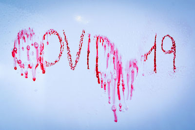 Close-up of heart shape with pink water drops against white background