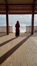 Rear view of woman walking on wooden railing against sky