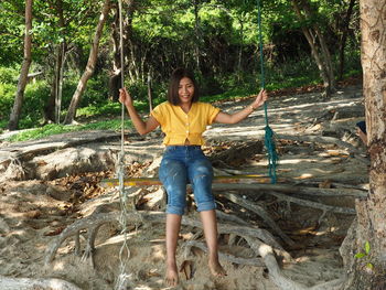 Full length portrait of smiling woman standing by tree