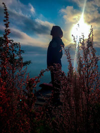 Side view of silhouette girl standing by tree against sky
