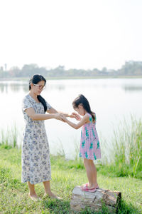 Full length of mother and daughter standing at riverbank against clear sky