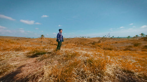 Side view of man standing on field against sky