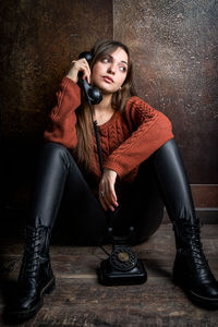 Portrait of young woman with telephone sitting on floor