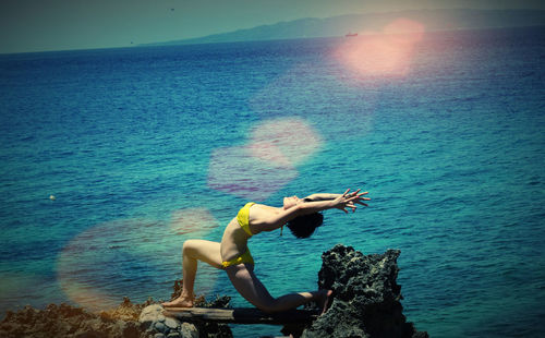 Full length of woman exercising against sea on sunny day