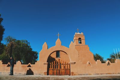 Man standing by church against clear blue sky