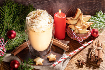 Christmas drink eggnog with whipped cream in glass, candle, fir branches, spices, xmas decorations.