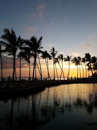 Silhouette palm trees by swimming pool against sky during sunset