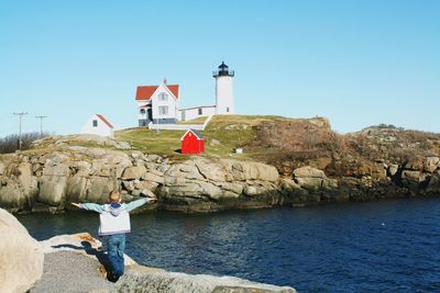 Rear view of boy standing with arms outstretched on rock by sea