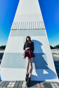 Full length portrait of young woman against blue sky