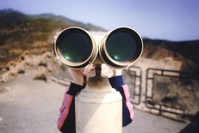 Cropped hand holding binoculars against sky