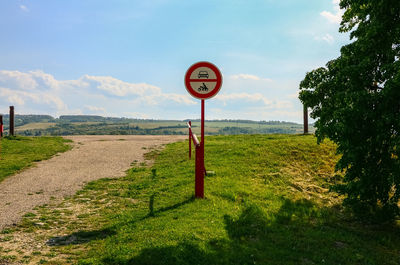 Road sign by trees on field against sky