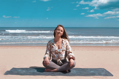 Young woman sitting at beach against sky