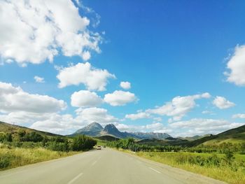 Empty road amidst field against sky