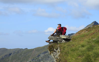 Low angle view of hiker sitting on rock against sky