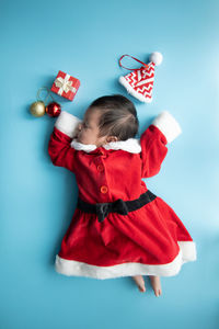 Directly above shot of baby girl wearing santa claus costume sleeping on blue background