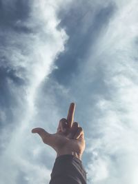 Cropped image of hand showing obscene gesture against cloudy sky